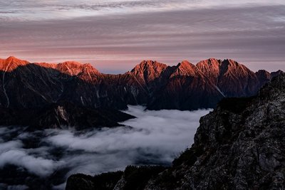 Untergehende Sonne hüllte Spitzen der Bergkette in warmes Licht während Nebel durchs Tal wabert