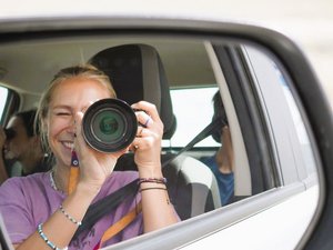 Frau fotografiert sich selbst im Seitenspiegel eines Mietwagens