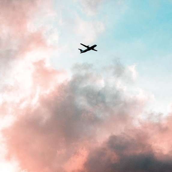 Flugzeug zwischen rosa Wolken und hellblauem Himmel