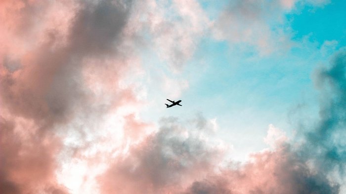 Flugzeug zwischen rosa Wolken und hellblauem Himmel
